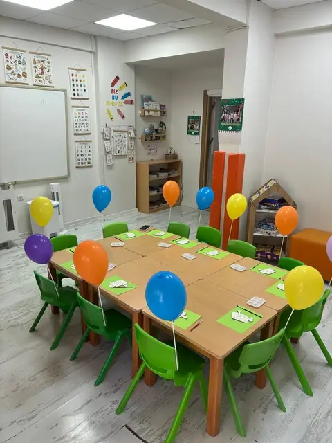 Balonlarla süslenmiş masa ve yeşil sandalyelerle sınıf